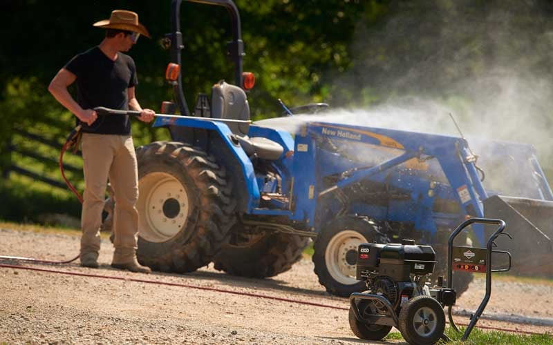 Man cleaning a blue tractor with Briggs & Stratton pressure washer.